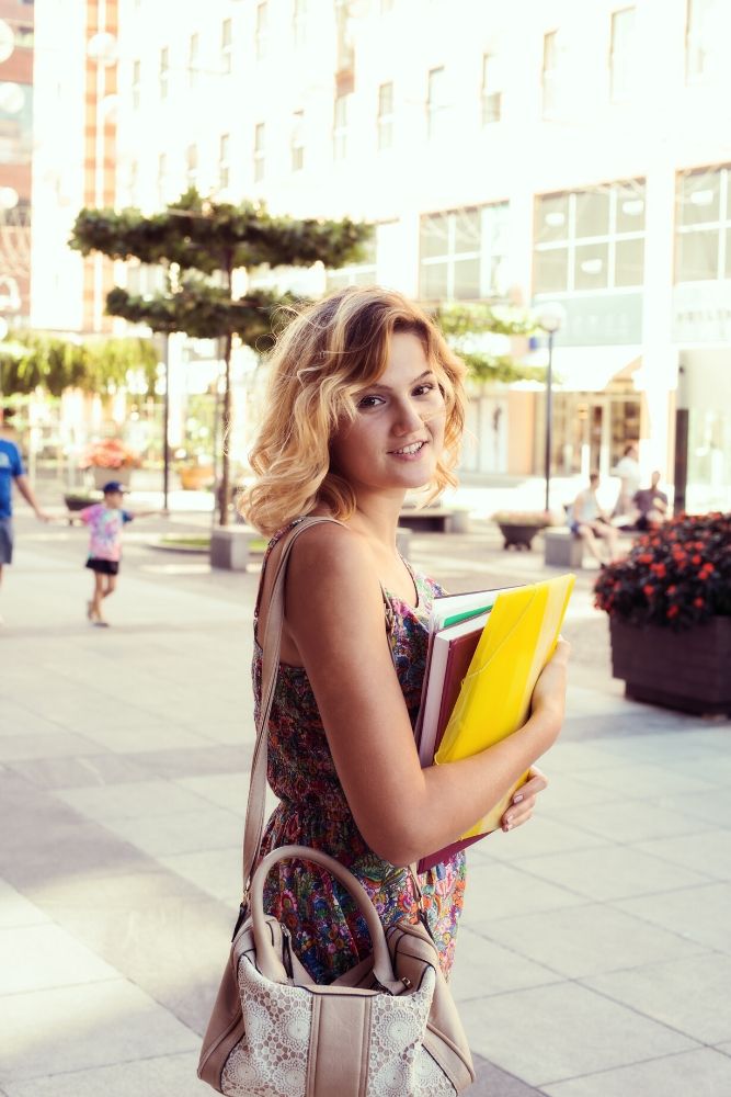 Chica con libros en la mano camina por la calle de camino a la universidad
