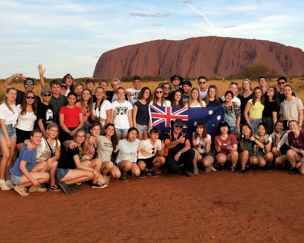 chicos con bandera australiana en el desierto frente a ayers rock