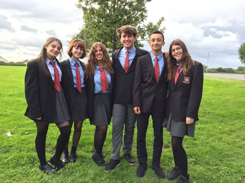 Due studenti e quattro studentesse irlandesi con un’uniforme scolastica nera, grigia, azzurra e rossa posano su un prato
