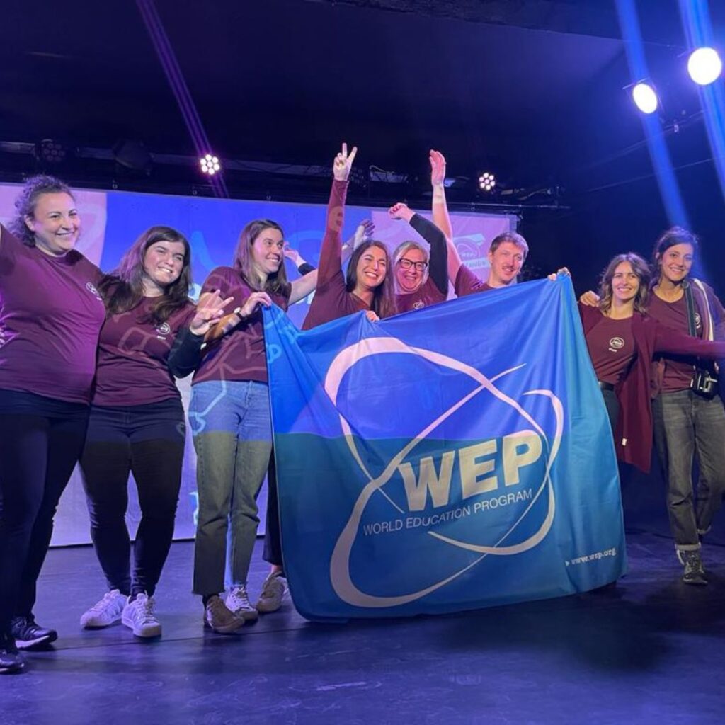 groupe composé de membres de l'équipe WEP, sur une scène, tenant un drapeau WEP pendant l'évènement pré-départ pour les jeunes partant en programme scolaire