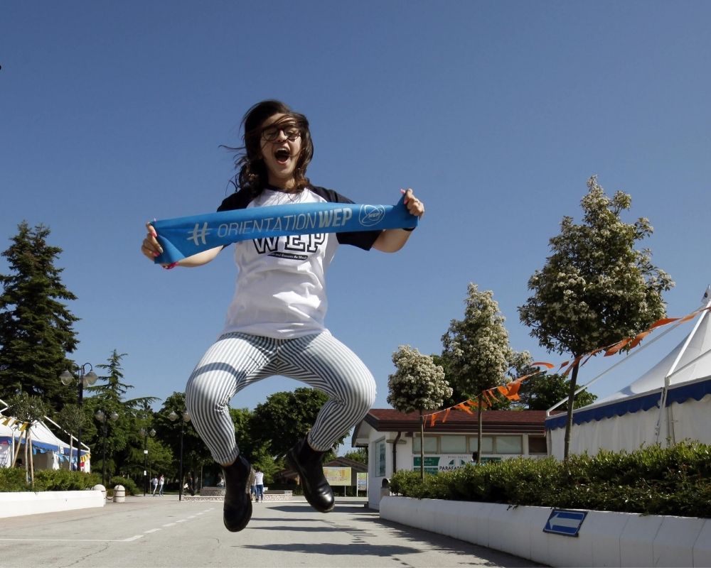 Une participante WEP saute avec un bandeau WEP bleu entre les mains pendant la formation pré-depart de WEP avant son programme scolaire à l'étranger.