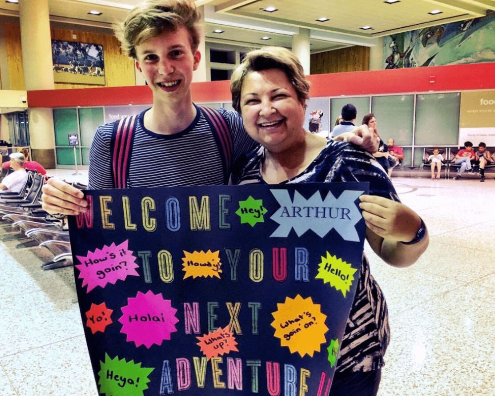 abbraccio famiglia studente con cartello benvenuto aeroporto