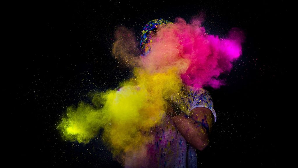 Holi Festival India - nuvola di colori giallo e rosa lanciata da una persona che non si vede su sfondo nero