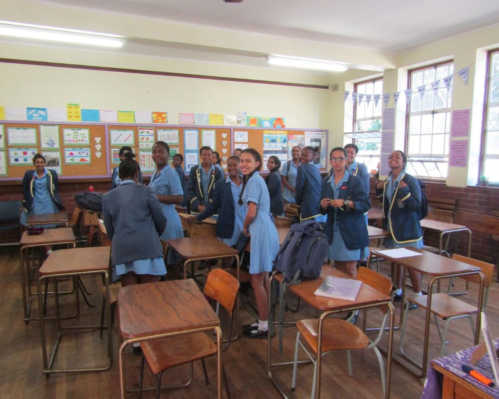 Studentesse di una scuola sudafricana con divisa scolastica, in piedi intorno ai banchi della classe