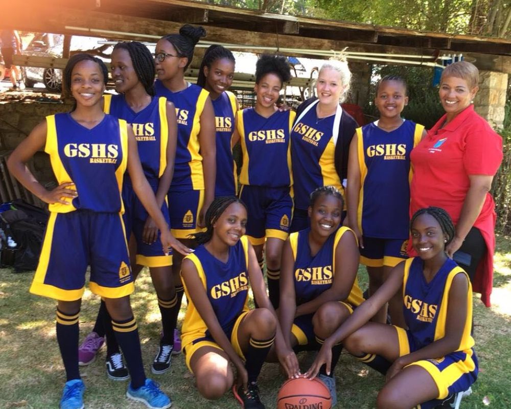 Ragazze di una squadra di basket sudafricana con divisa viola e gialla insieme all’allenatrice