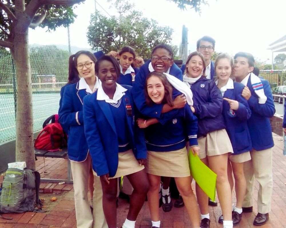 Gruppo di studenti sudafricani con divisa blu e beige vicino a un campo sportivo della scuola