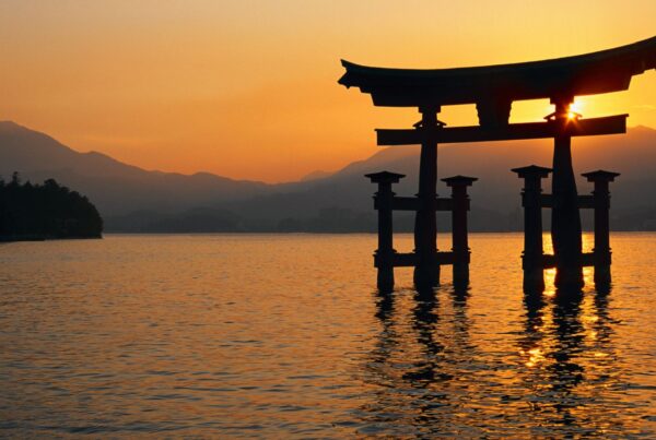 Il profilo nero di un tipico portale giapponese che delinea un’area sacra; la struttura è immersa nell’acqua, circondata dalla luce calda del tramonto