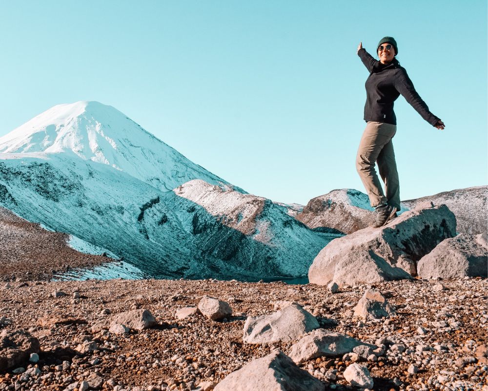 Sulla destra una ragazza in abbigliamento sportivo su una roccia tra sassi grigi; sullo sfondo cielo azzurro e sulla sinistra alta montagna innevata