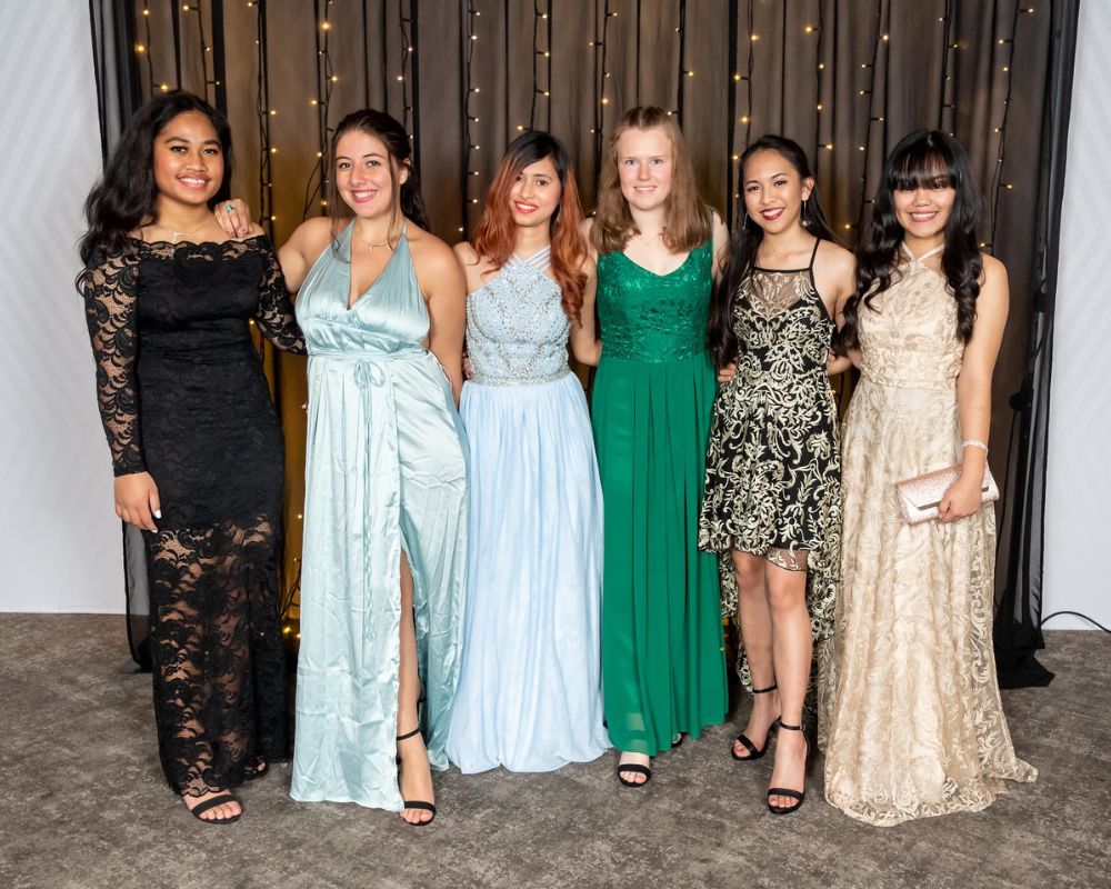 Studentesse neozelandesi in abiti eleganti posano per la foto del ballo scolastico. Indossano abiti da sera con gonne fino ai piedi e sandali neri con il tacco