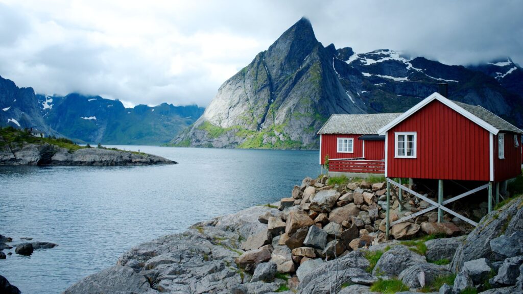 Fiordo norvegese: lingua di mare che si insinua in grigie montagne rocciose. Sulla destra una palafitta di legno dipinta di rosso con finestre bianche