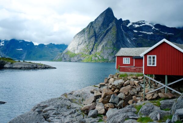 Fiordo norvegese: lingua di mare che si insinua in grigie montagne rocciose. Sulla destra una palafitta di legno dipinta di rosso con finestre bianche