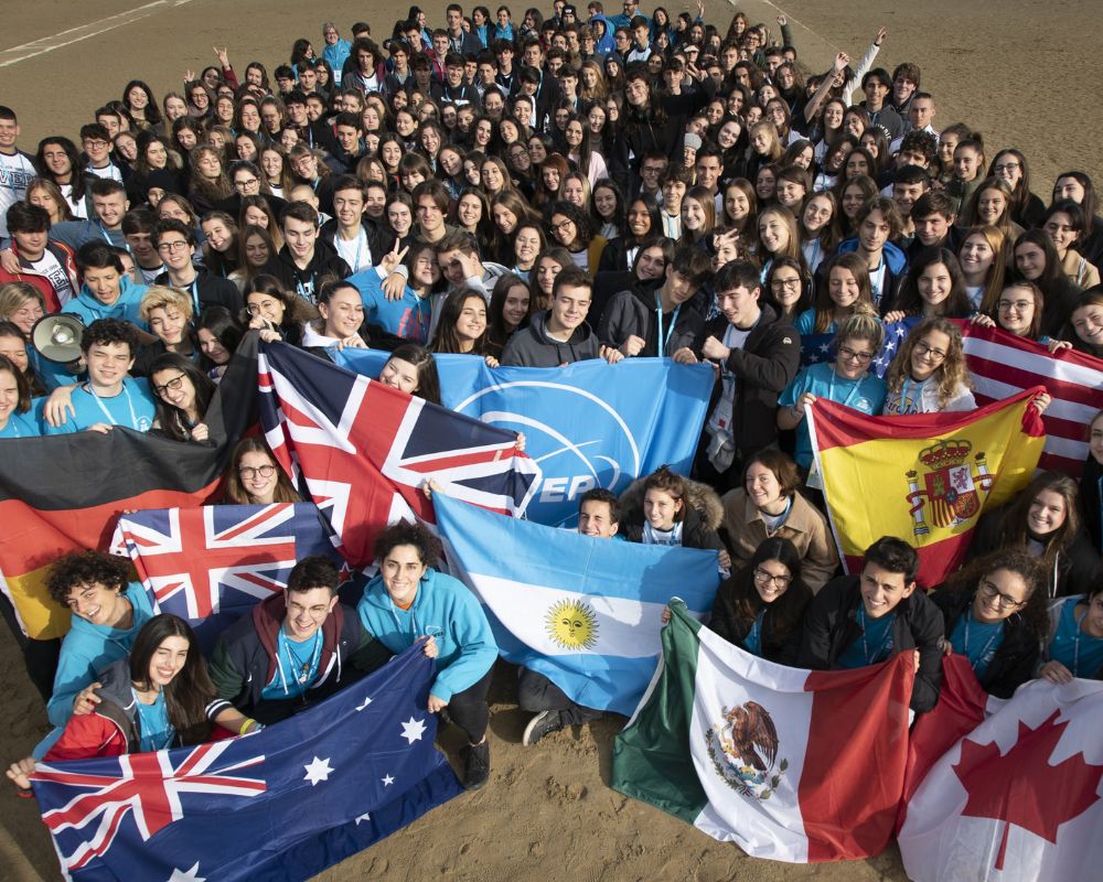 Ripresa dall’alto di studenti con bandiere di Paesi anglofoni, ispanofoni e tedescofoni all’Orientation WEP, pronti per l’anno all’estero