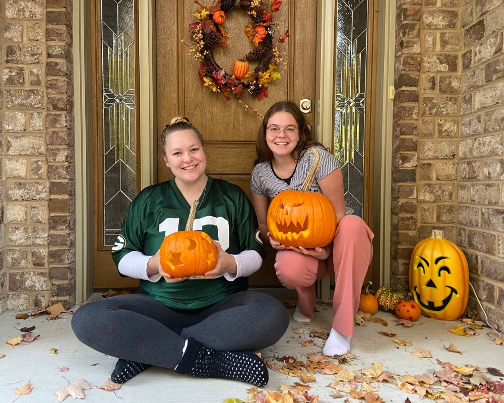 Due ragazze con zucche intagliate tra le braccia, in posa davanti alla porta di casa addobbata in America per Halloween