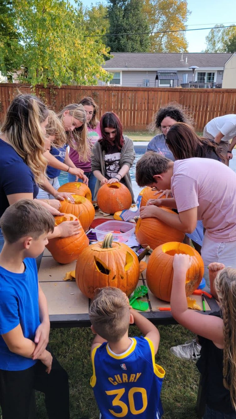 Bambini, ragazzi e genitori intagliano zucche per Halloween intorno a un tavolo