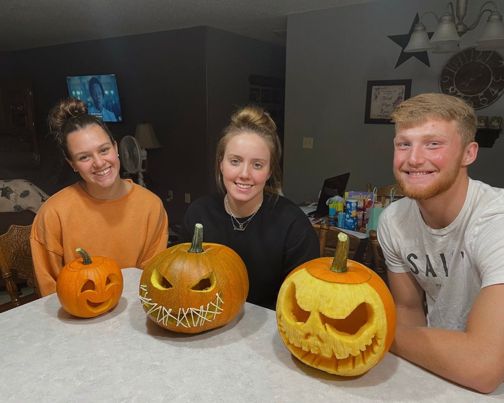 Due ragazze e un ragazzo sorridono con le loro zucche intagliate per Halloween