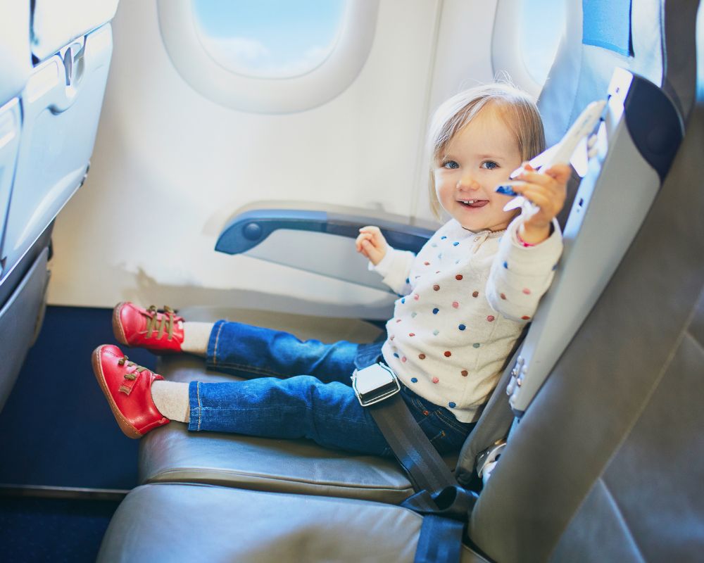 Cosa fare in aereo per passare il tempo: una bambina con caschetto biondo, jeans e maglietta bianca gioca con aereo giocattolo