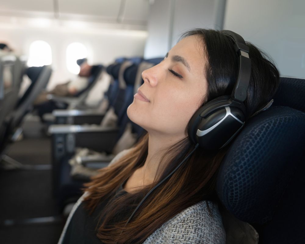 Cosa fare in aereo per passare il tempo: una ragazza con capelli lunghi scuri ascolta musica o podcast con cuffie