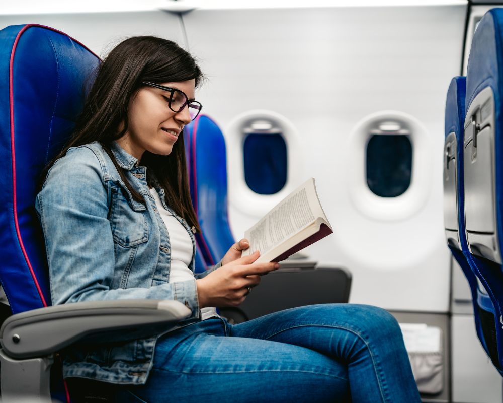 Cosa fare in aereo per passare il tempo: una giovane con capelli lunghi neri legge un libro