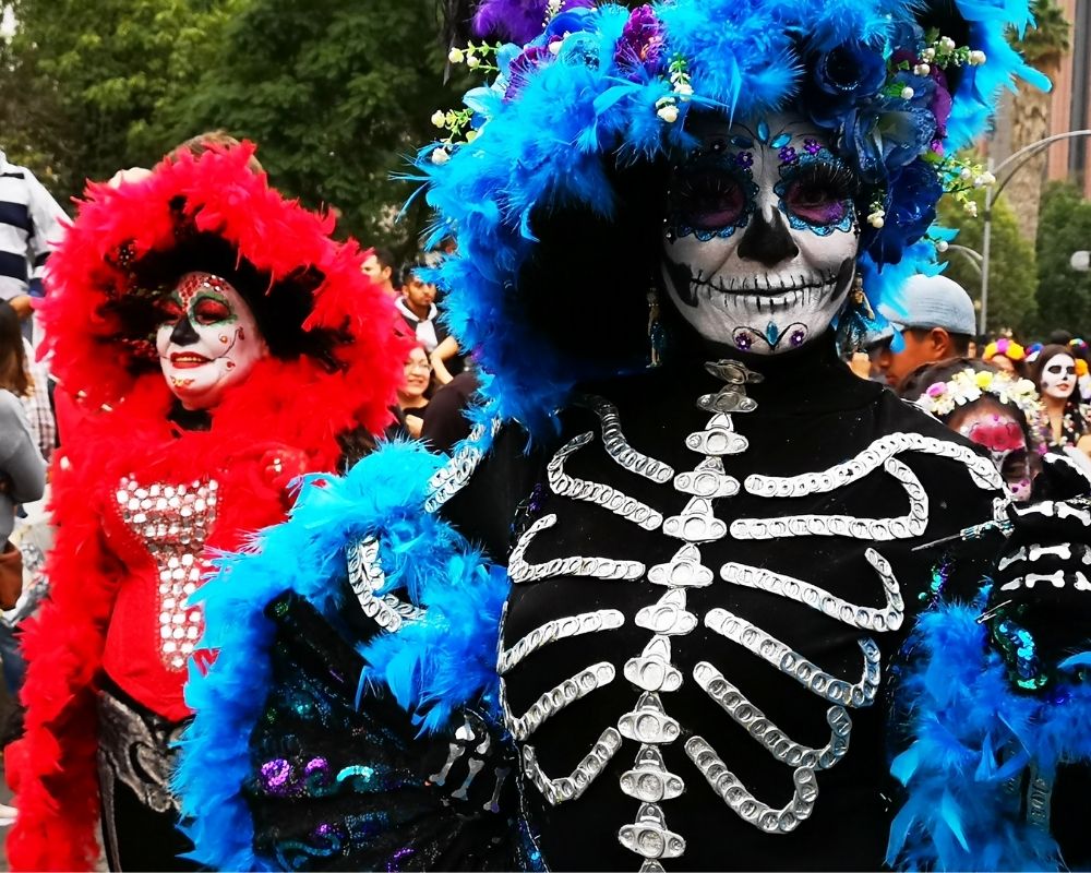 Sfilata in maschera in occasione della Festa dei Morti in Messico: piume rosse e blu, scheletri e paillettes