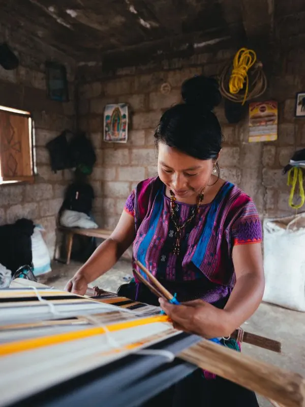 Una donna messicana lavora al telaio a mano. Indossa un abito a maniche corte a strisce verticali azzurre e viola