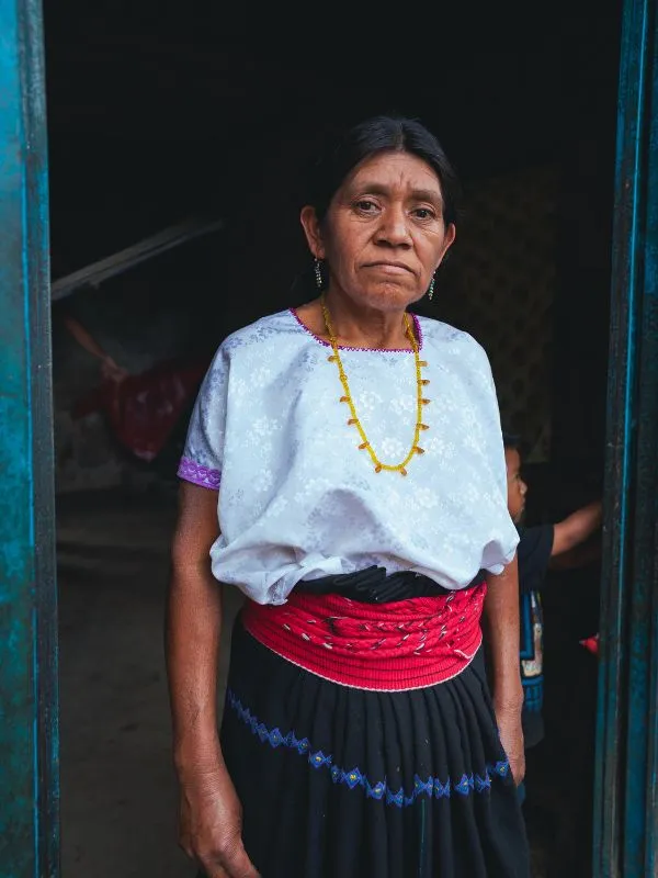 Una donna dai tipici lineamenti maya indossa una camicia in seta bianca e una gonna scura, con spessa cintura rossa