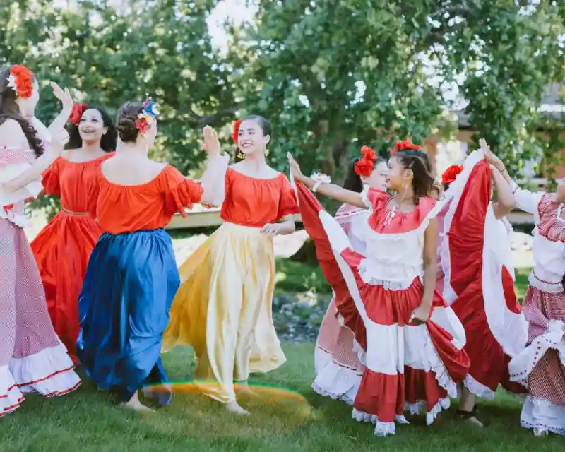 Un gruppo di donne in colorati abiti dellaadizione messicana con ampie gonne e camicette danzano sorridenti a ritmo di cumbia