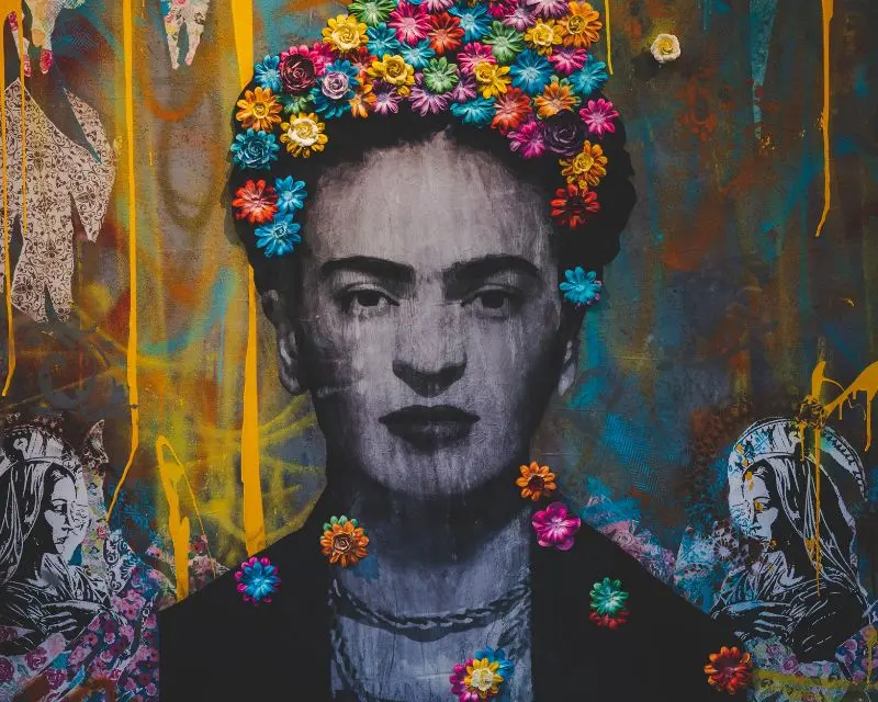 Murale con un primo piano scuro di Frida Kahlo con piccoli fiori colorati in testa