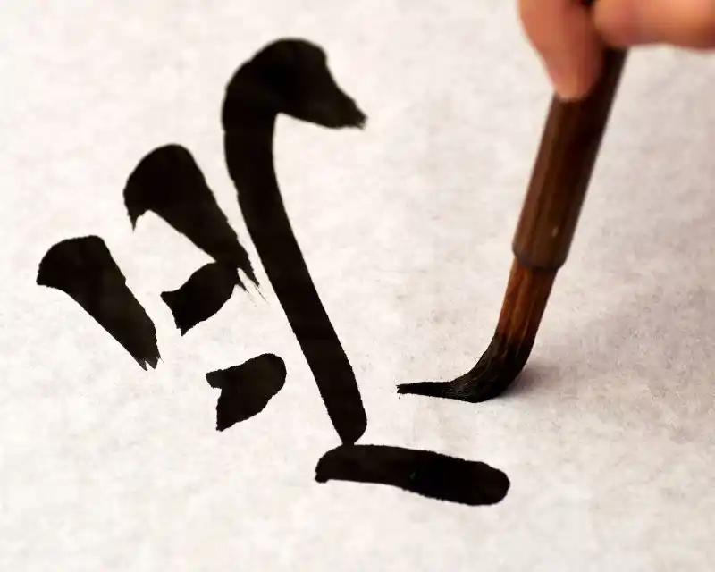 Punta di pennello con pittura nera che delinea su un foglio di carta a righe un logogramma giapponese