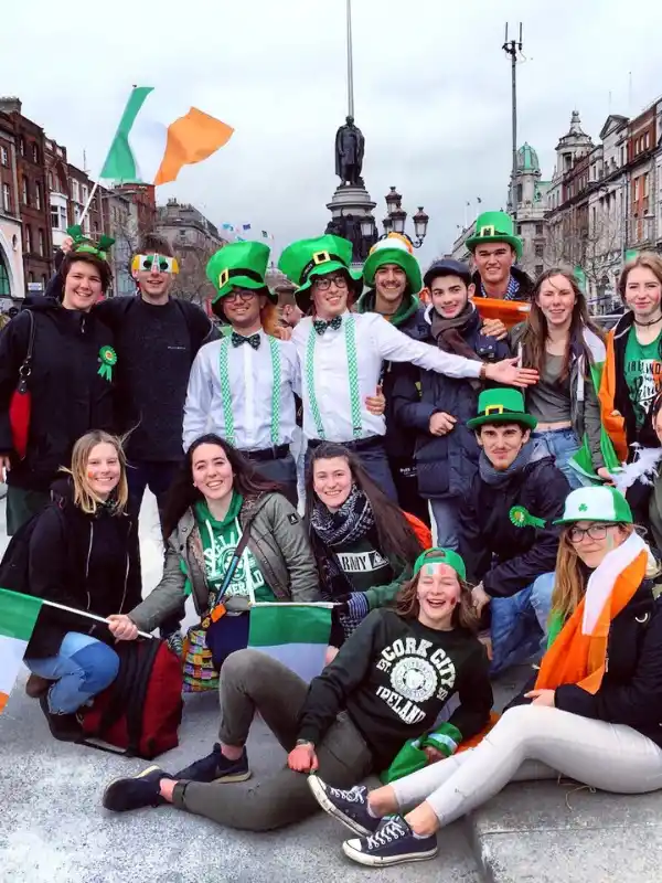 Gruppo di ragazzi e ragazze con bandiere irlandesi e cappelli verdi in posa in una strada irlandese per la festa di San Patrizio