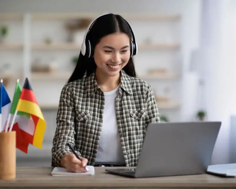 Imparare il giapponese online: ragazza asiatica al computer con cuffie che prende appunti su un quaderno