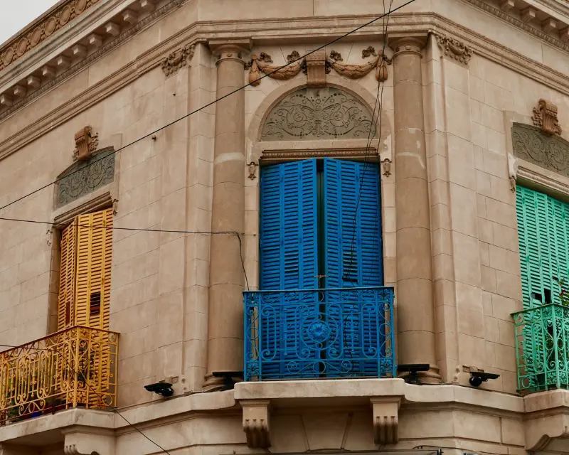 Palazzo neoclassico di Buenos Aires con 3 finestre e balconi dipinti in colori sgargianti in contrasto con il muro sobrio retrostante