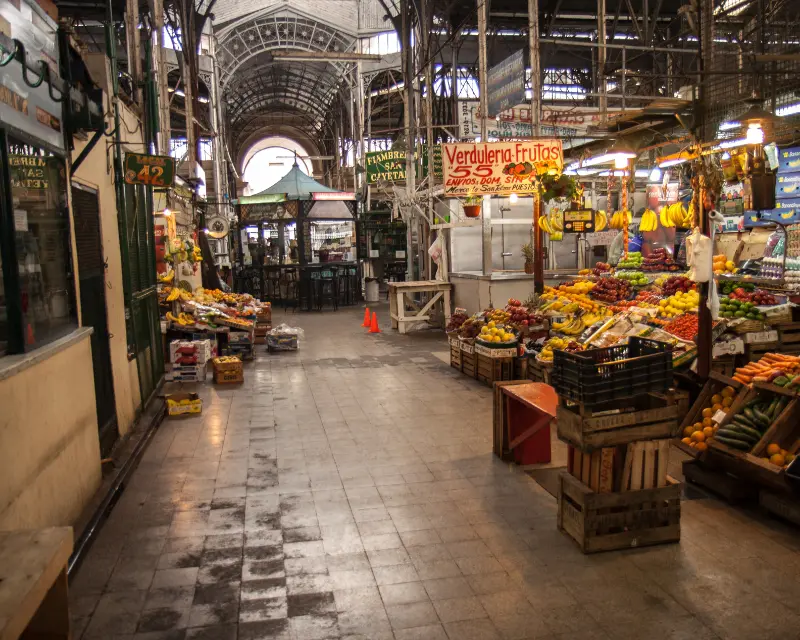 Interno di un mercato argentino con frutta e verdura esposti sui banchi sotto una copertura in ferro