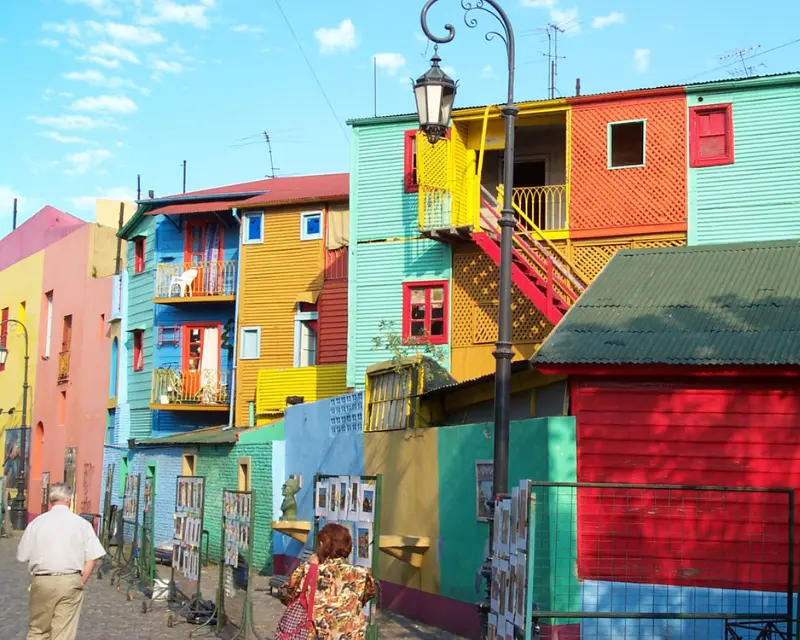 Vista dalla strada di alcune case a 2 o 3 piani molto colorate con sedie sui balconi a Buenos Aires. Lungo la strada delle foto o disegni sono esposti su dei pannelli