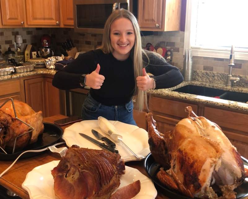 Ragazza fa i pollici in alto e sul tavolo di fronte a lei ci sono tacchini arrosto e prosciutto arrosto pronti per essere consumati durante il Thanksgiving