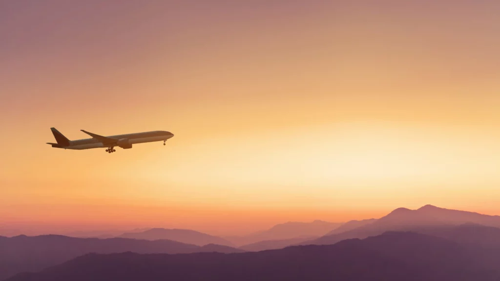 Aereo che vola sopra una catena montuosa al tramonto, con il carrello d’atterraggio già abbassato