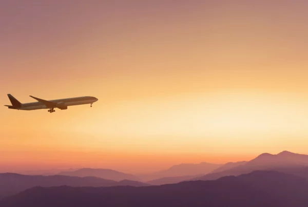 Aereo che vola sopra una catena montuosa al tramonto, con il carrello d’atterraggio già abbassato