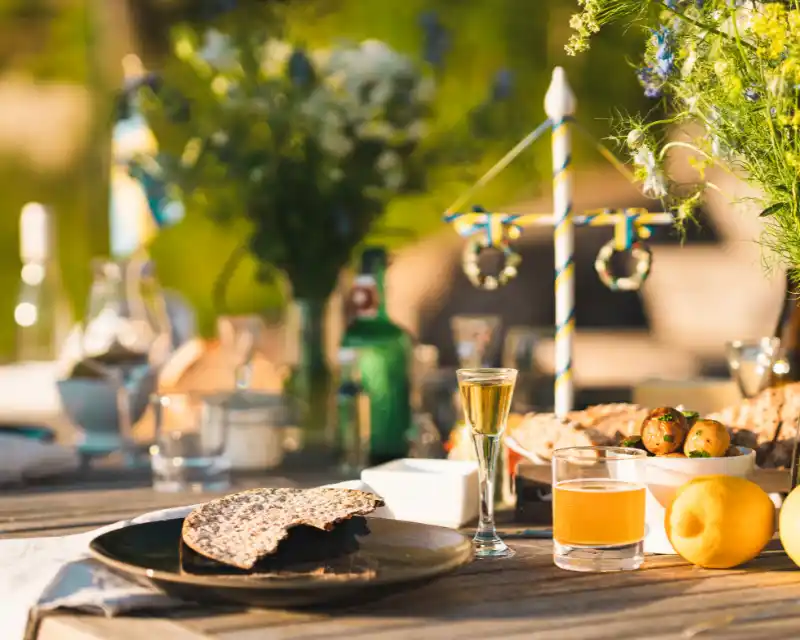 Durante il Midsommar, le tavole si riempiono di piatti tipici come pane croccante, patate novelle e aquavit, tra fiori di campo e simboli tradizionali