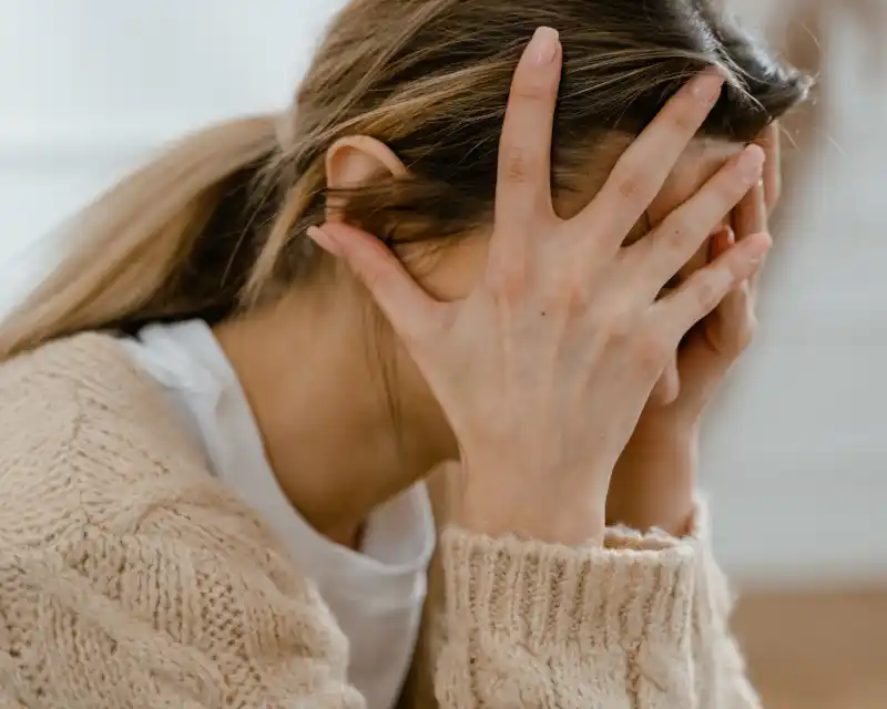 Una donna siede con il viso tra le mani, visibilmente provata: un'immagine che racconta la difficoltà emotiva di chi vive la nostalgia di un figlio lontano da casa.