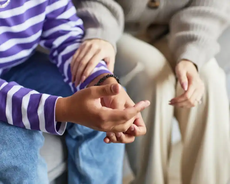 Primo piano di mani intrecciate: un gesto semplice e profondo che racconta la vicinanza e il supporto tra genitore e figlio, anche quando il figlio è lontano da casa.