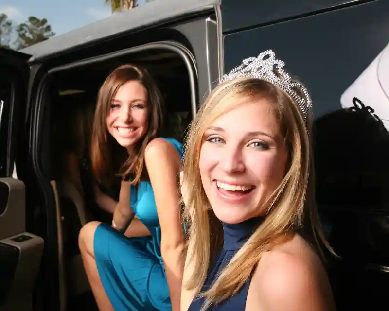 Due ragazze in vestiti da ballo di fine anno posano davanti a una limousine. Il Prom americano è una serata da sogno.