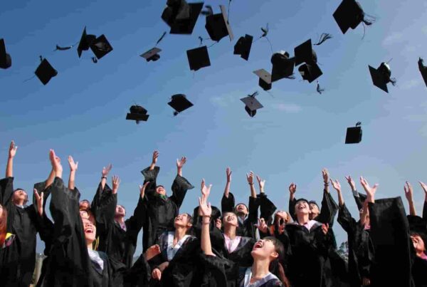 Studenti in toga e graduation cap lanciano i cappelli in aria durante la cerimonia di diploma americano all’aperto.