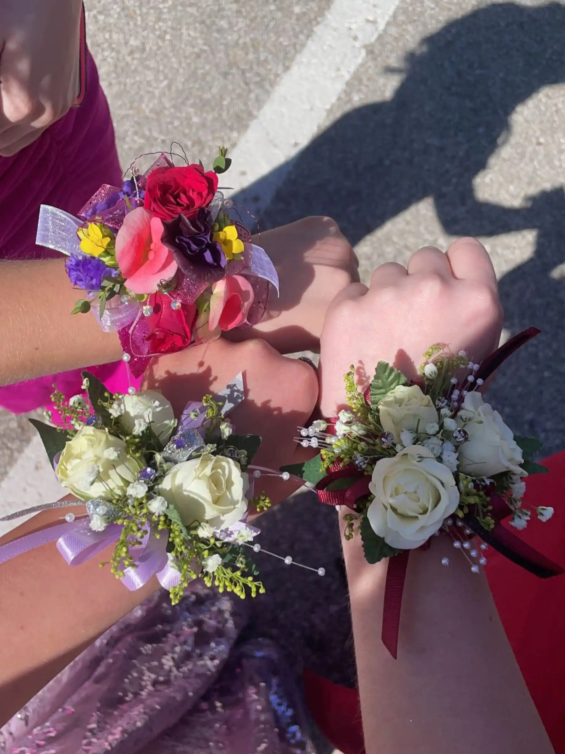 Tre corsage colorati con rose e nastri decorano i polsi delle ragazze, un dettaglio tipico dei vestiti da ballo di fine anno.