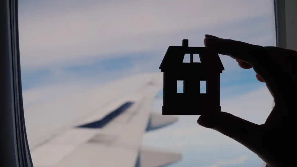 Una casa di carta contro il cielo: simbolo visivo potente della nostalgia di casa all’inizio di un’esperienza all’estero.