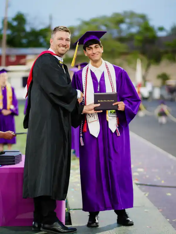 Studente in toga viola stringe la mano al preside durante la cerimonia del graduation day negli USA.
