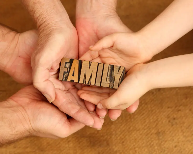 Mani di adulti e bambini che si stringono attorno alla parola “Family”, simbolo di affetto e del rapporto genitori figli.