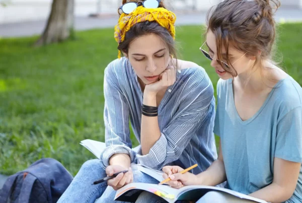 Ragazze sedute vicino a un prato fanno degli esercizi di grammatica su un libro di testo per imparare il tedesco