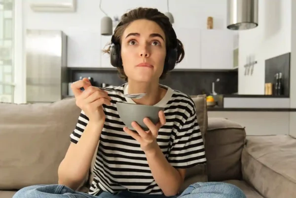 Ragazza con le cuffie e una maglietta a righe a maniche corte guarda una serie TV in tedesco mentre mangia dei cereali