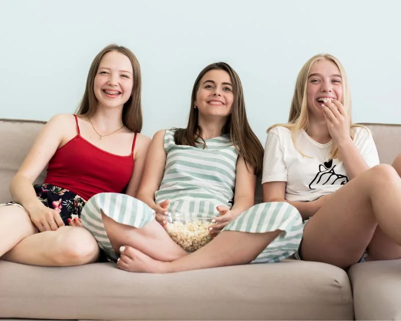 Tre amiche delle scuole medie con i capelli lisci guardano una serie TV divertente in tedesco con i sottotitoli in italiano