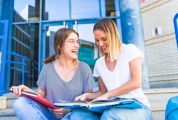 Due ragazze che si sono trasferite in Germania per l'anno all'estero stanno studiando i modi di dire in tedesco seduti sui gradini davanti alla scuola