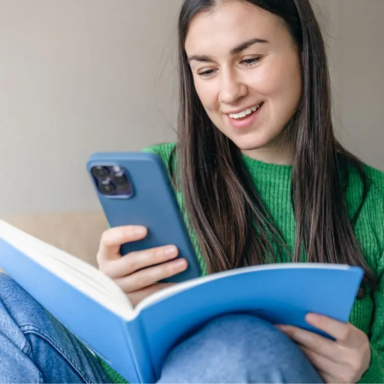 Ragazza quindicenne con maglione verde e libro in mano affianca lo studio del tedesco all'uso di un'app per imparare le lingue straniere.